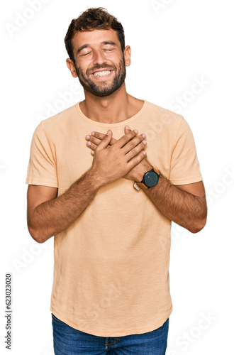 Handsome young man with beard wearing casual tshirt smiling with hands on chest with closed eyes and grateful gesture on face. health concept.