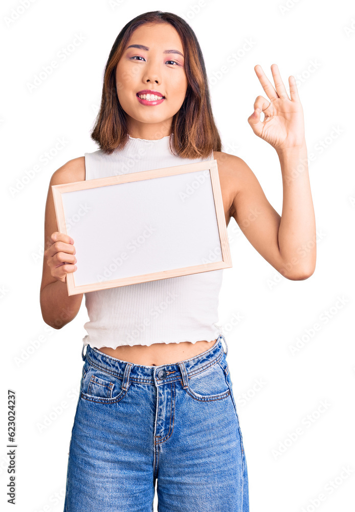 Young beautiful chinese girl holding empty white chalkboard doing ok sign with fingers, smiling friendly gesturing excellent symbol Young beautiful chinese girl holding empty white chalkboard doing ok sign with fingers, smiling friendly gesturing excellent symbol