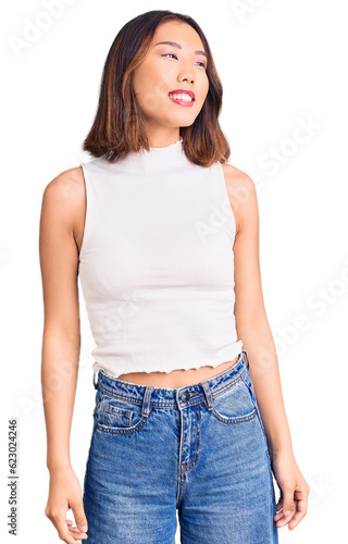 Young beautiful chinese girl wearing casual clothes looking away to side with smile on face, natural expression. laughing confident.