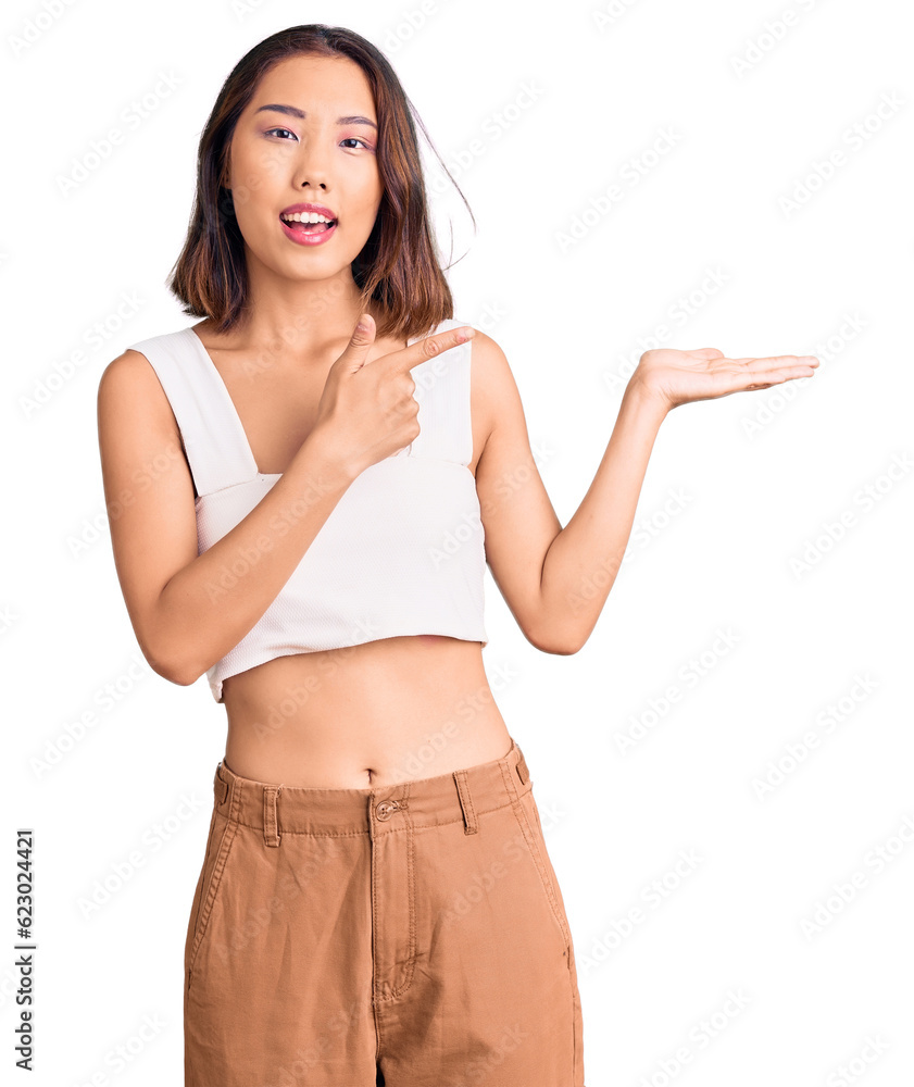 Young beautiful chinese girl wearing casual clothes amazed and smiling to the camera while presenting with hand and pointing with finger. Young beautiful chinese girl wearing casual clothes amazed and smiling to the camera while presenting with hand and pointing with finger.