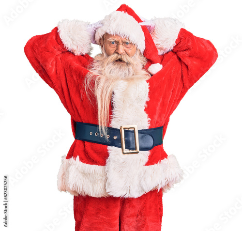 Old senior man with grey hair and long beard wearing traditional santa claus costume crazy and scared with hands on head, afraid and surprised of shock with open mouth