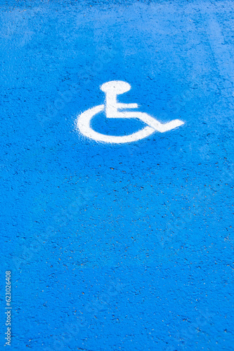 International symbol of reserved or preferential use for people with disabilities painted on the ground on a blue background.