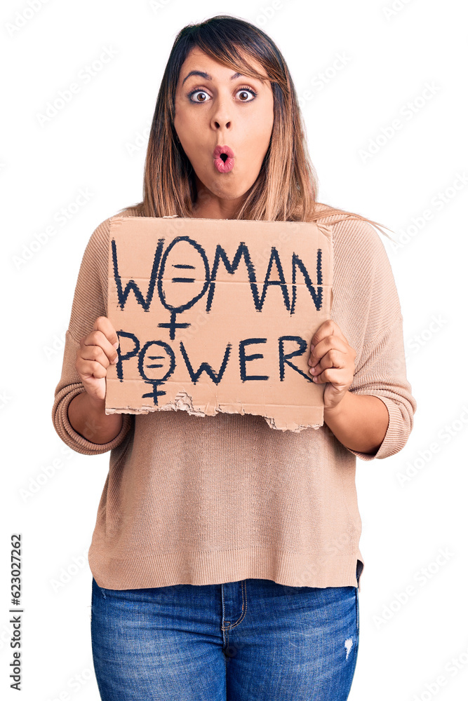 Young beautiful woman holding woman power banner scared and amazed with open mouth for surprise, disbelief face Young beautiful woman holding woman power banner scared and amazed with open mouth for surprise, disbelief face