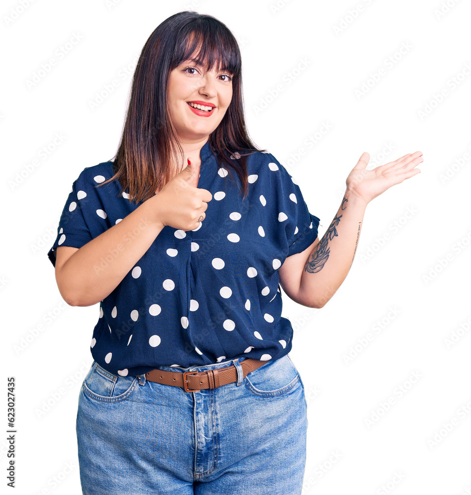 Young plus size woman wearing casual clothes showing palm hand and doing ok gesture with thumbs up, smiling happy and cheerful Young plus size woman wearing casual clothes showing palm hand and doing ok gesture with thumbs up, smiling happy and cheerful