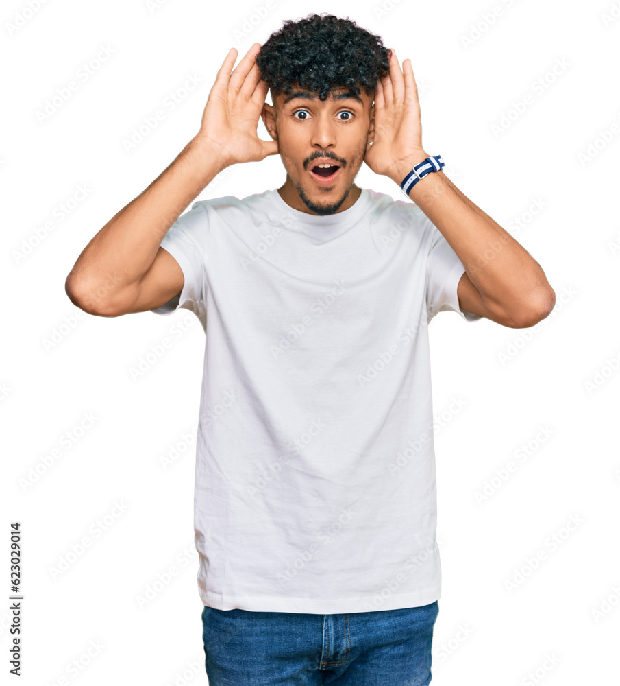 Young arab man wearing casual white t shirt smiling cheerful playing peek a boo with hands showing face. surprised and exited Young arab man wearing casual white t shirt smiling cheerful playing peek a boo with hands showing face. surprised and exited