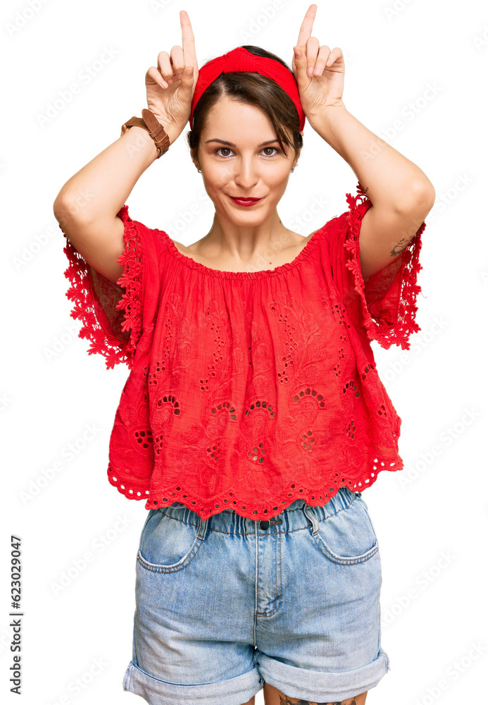Young brunette woman with short hair wearing casual summer clothes and diadem doing funny gesture with finger over head as bull horns Young brunette woman with short hair wearing casual summer clothes and diadem doing funny gesture with finger over head as bull horns