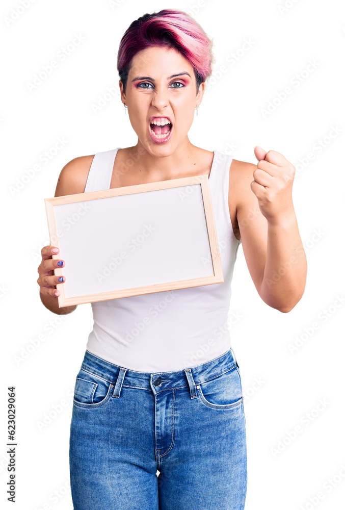 Young beautiful woman with pink hair holding empty white chalkboard annoyed and frustrated shouting with anger, yelling crazy with anger and hand raised Young beautiful woman with pink hair holding empty white chalkboard annoyed and frustrated shouting with anger, yelling crazy with anger and hand raised