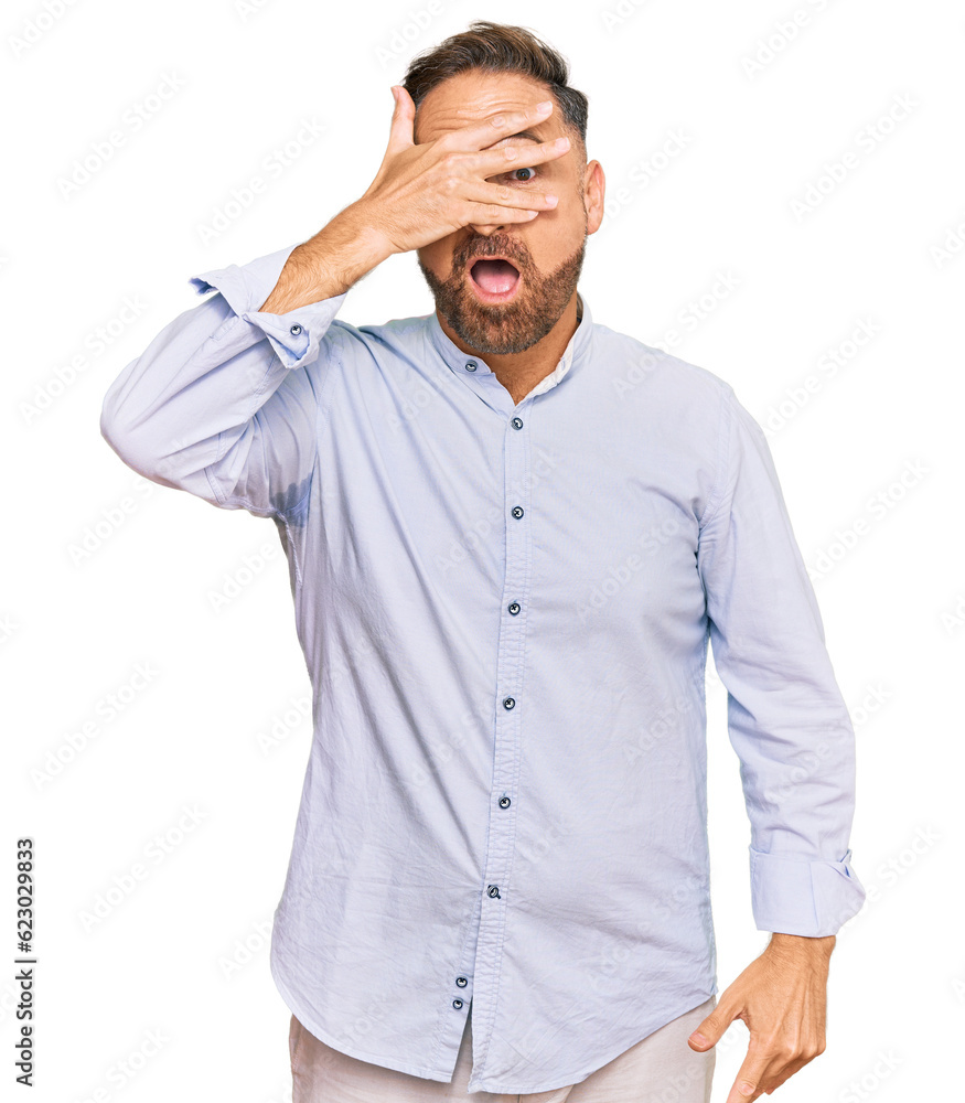 Handsome middle age man wearing business shirt peeking in shock covering face and eyes with hand, looking through fingers with embarrassed expression. Handsome middle age man wearing business shirt peeking in shock covering face and eyes with hand, looking through fingers with embarrassed expression.