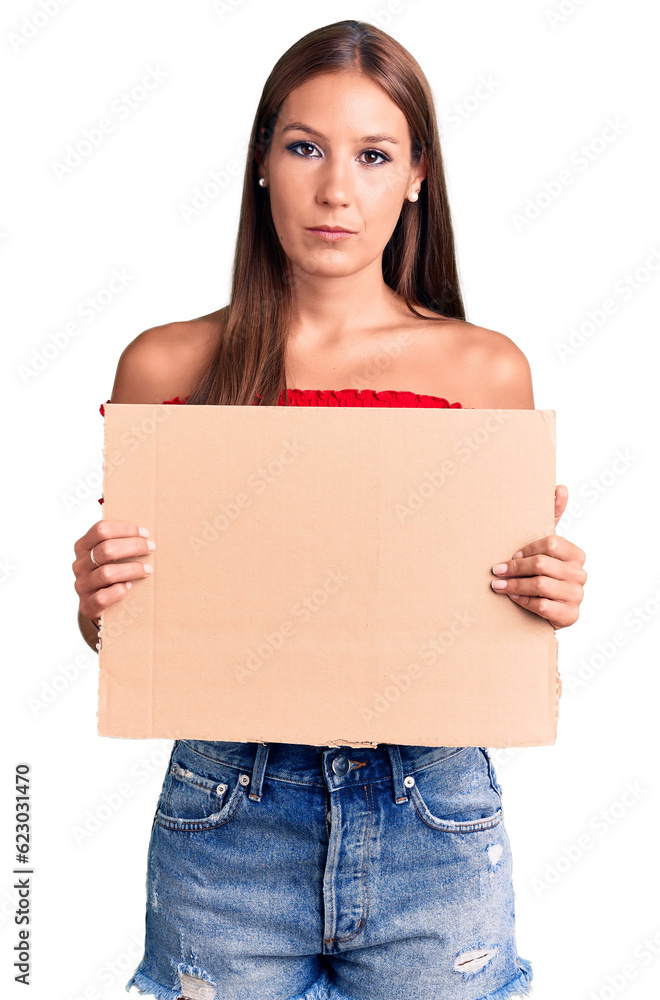 Young beautiful hispanic woman holding banner cardboard thinking attitude and sober expression looking self confident Young beautiful hispanic woman holding banner cardboard thinking attitude and sober expression looking self confident
