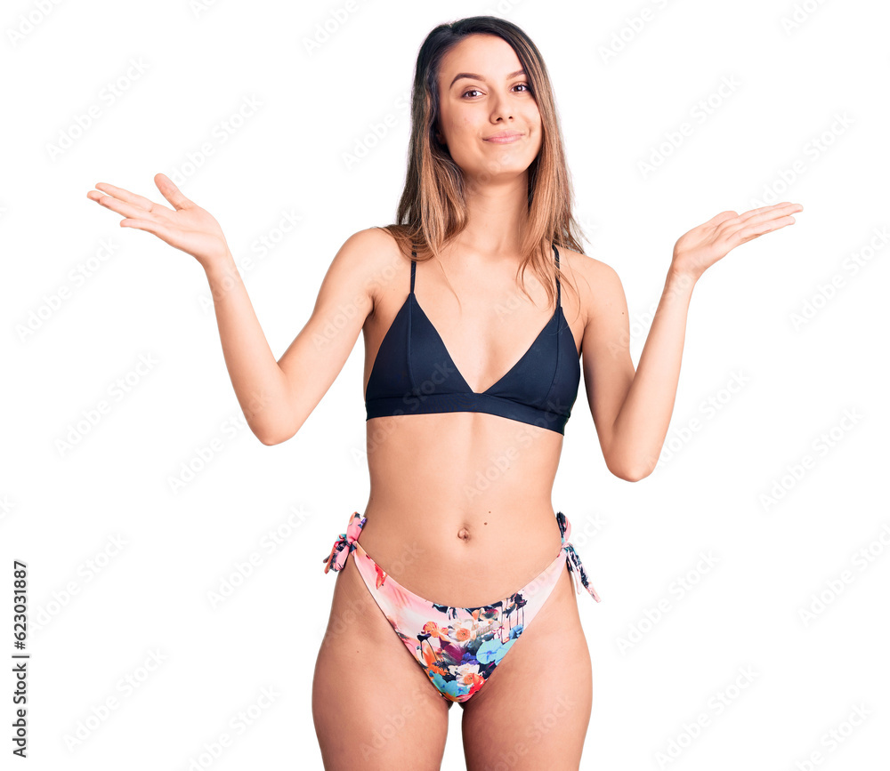 Young beautiful girl wearing bikini clueless and confused expression with arms and hands raised. doubt concept. Young beautiful girl wearing bikini clueless and confused expression with arms and hands raised. doubt concept.