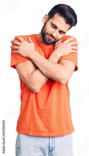 Young handsome man with beard wearing casual t-shirt hugging oneself happy and positive, smiling confident. self love and self care