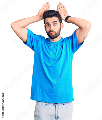 Young handsome man with beard wearing casual t-shirt doing bunny ears gesture with hands palms looking cynical and skeptical. easter rabbit concept.