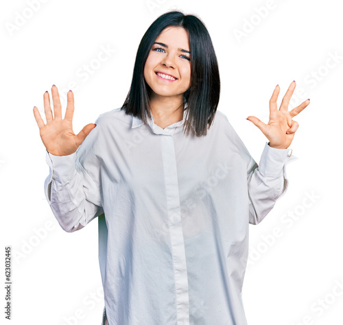 Young brunette woman with blue eyes wearing oversize white shirt showing and pointing up with fingers number nine while smiling confident and happy.