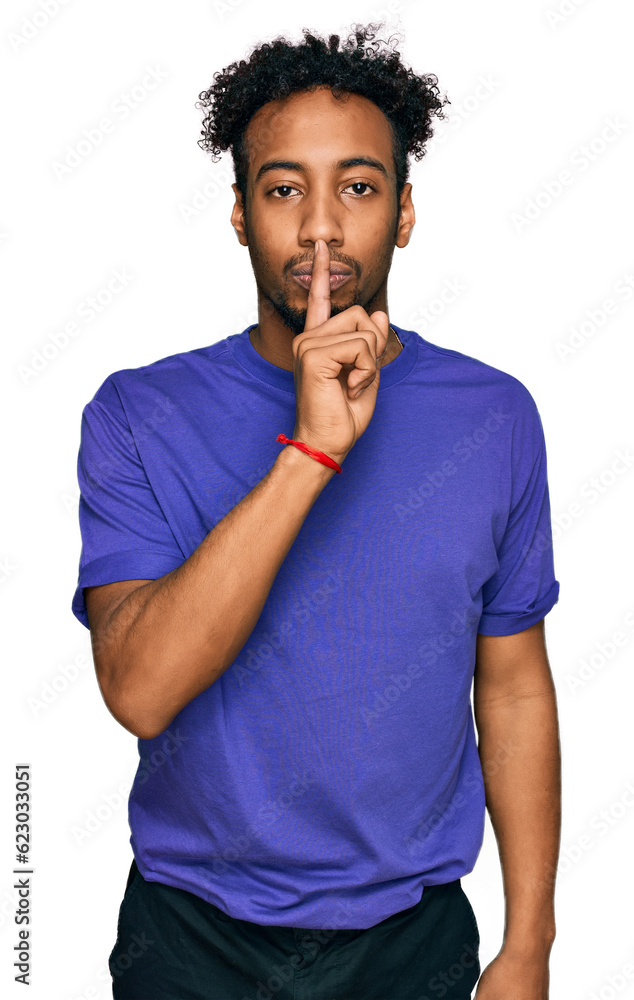 Young african american man with beard wearing casual purple t shirt asking to be quiet with finger on lips. silence and secret concept. Young african american man with beard wearing casual purple t shirt asking to be quiet with finger on lips. silence and secret concept.
