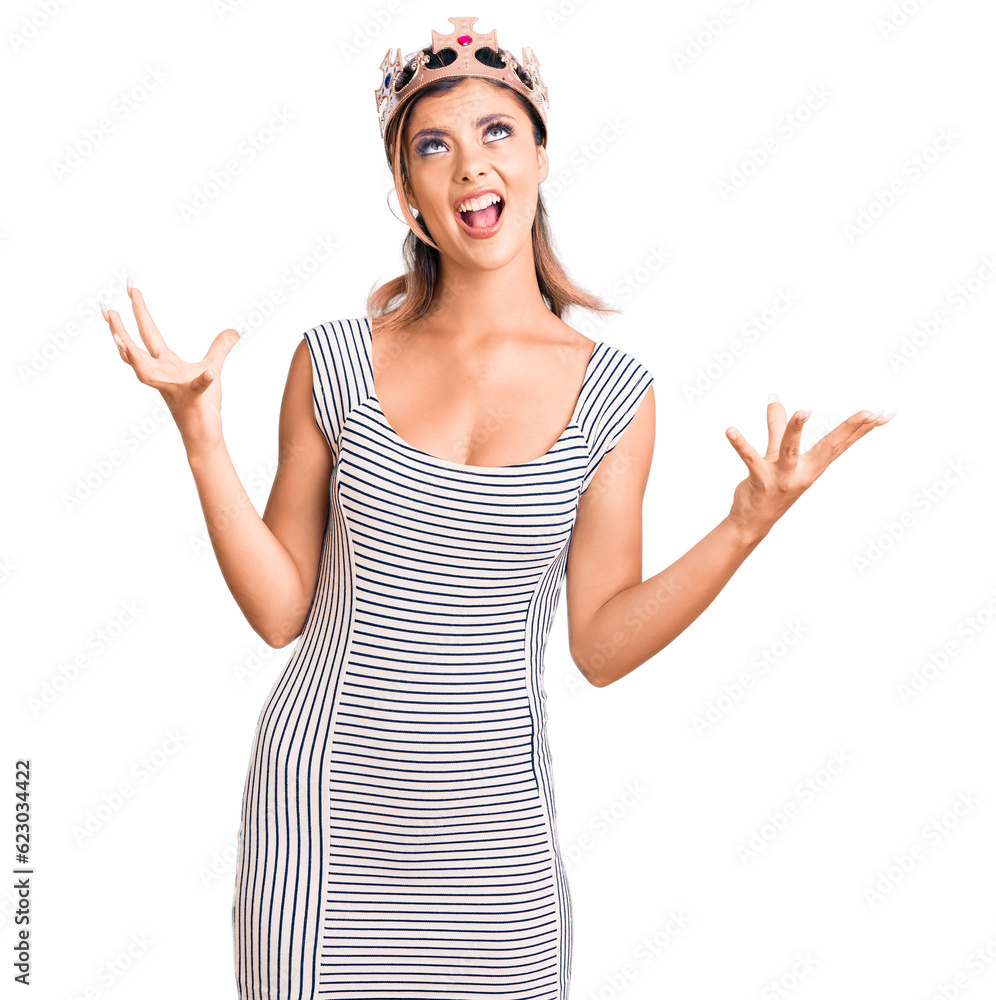 Young beautiful woman wearing king crown crazy and mad shouting and yelling with aggressive expression and arms raised. frustration concept.