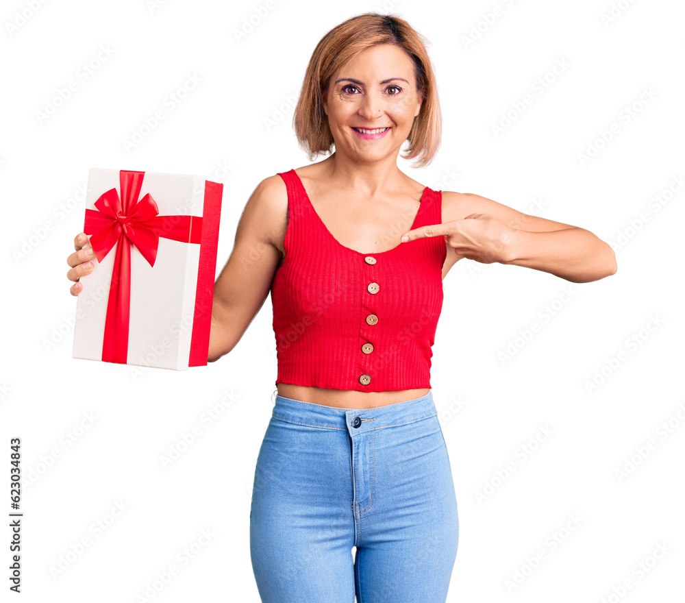 Young blonde woman holding gift pointing finger to one self smiling happy and proud Young blonde woman holding gift pointing finger to one self smiling happy and proud