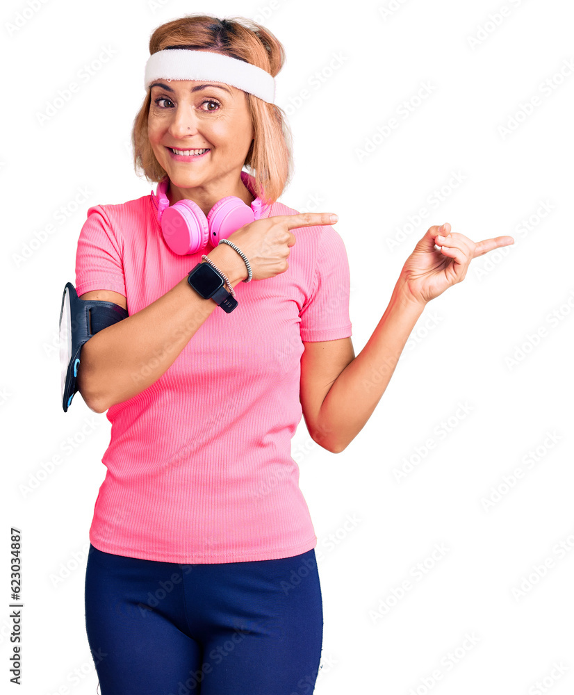 Young blonde woman wearing sportswear and headphones smiling and looking at the camera pointing with two hands and fingers to the side. Young blonde woman wearing sportswear and headphones smiling and looking at the camera pointing with two hands and fingers to the side.