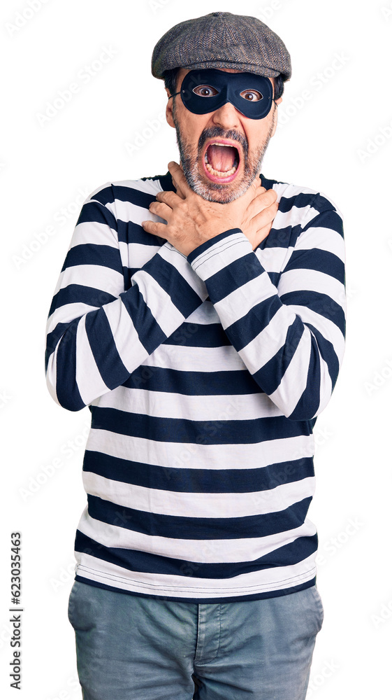 Middle age handsome man wearing burglar mask shouting and suffocate because painful strangle. health problem. asphyxiate and suicide concept. Middle age handsome man wearing burglar mask shouting and suffocate because painful strangle. health problem. asphyxiate and suicide concept.