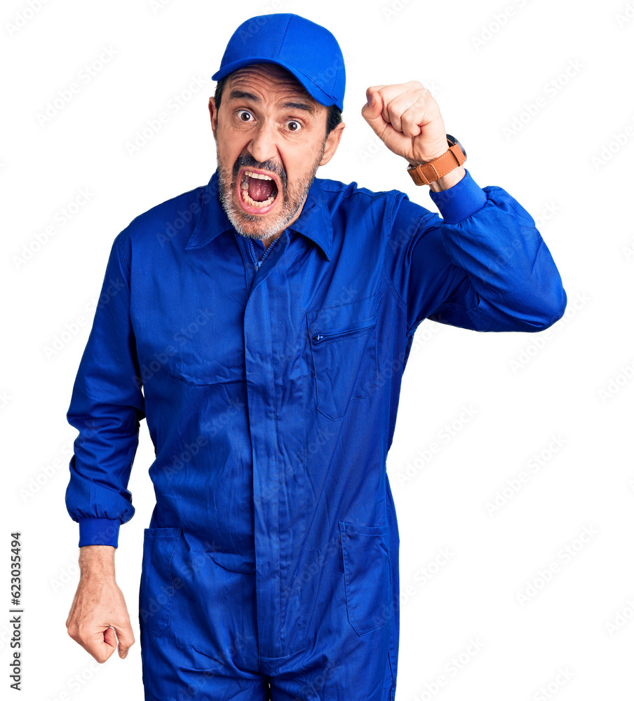 Middle age handsome man wearing mechanic uniform angry and mad raising fist frustrated and furious while shouting with anger. rage and aggressive concept.