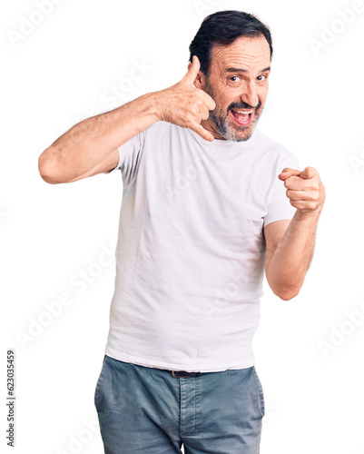 Middle age handsome man wearing casual t-shirt smiling doing talking on the telephone gesture and pointing to you. call me.