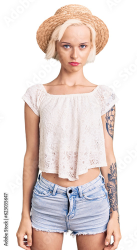 Young blonde woman with tattoo wearing summer hat depressed and worry for distress, crying angry and afraid. sad expression.