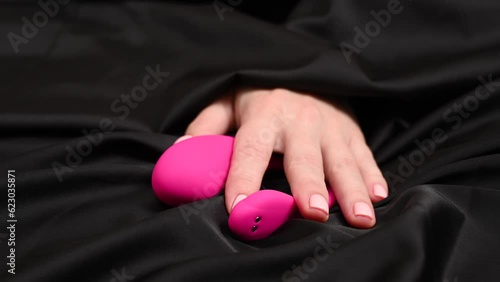 Woman taking a pink vibrator lying on a black silk sheet. 