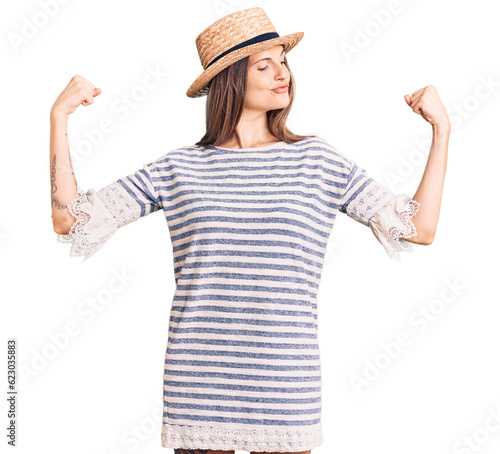 Beautiful caucasian woman wearing summer hat showing arms muscles smiling proud. fitness concept.