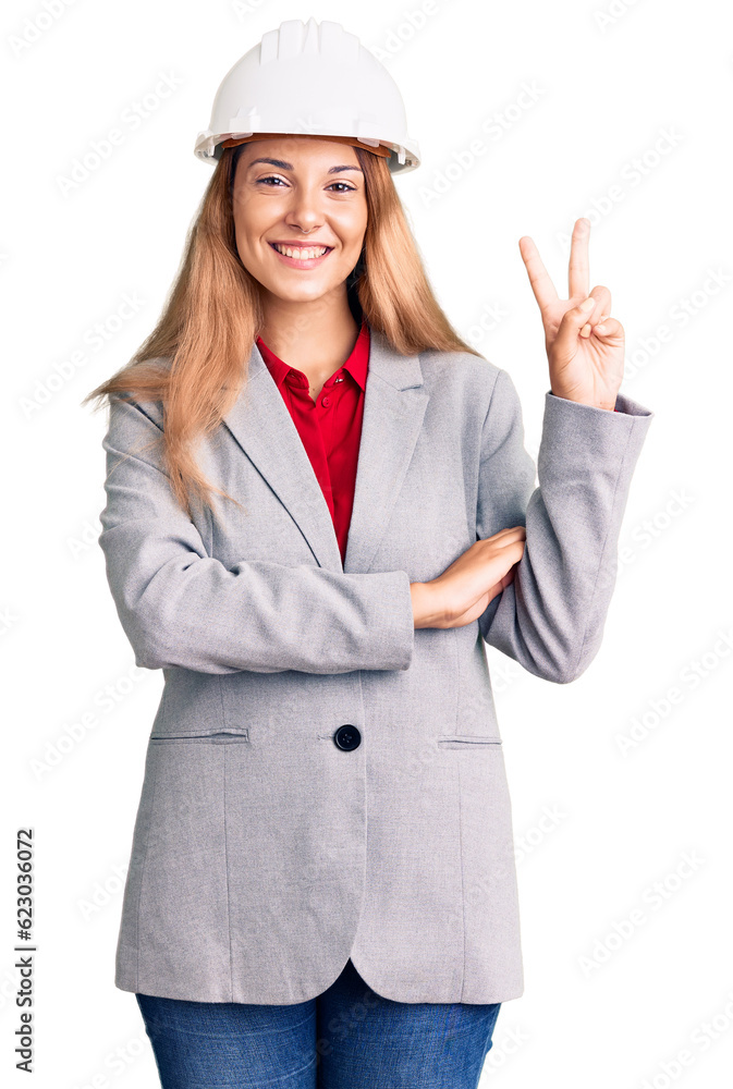 Beautiful young woman wearing architect hardhat smiling with happy face winking at the camera doing victory sign. number two. Beautiful young woman wearing architect hardhat smiling with happy face winking at the camera doing victory sign. number two.