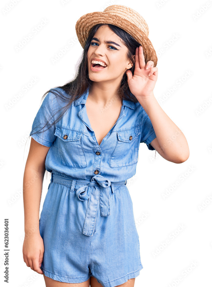 Brunette teenager girl wearing summer hat smiling with hand over ear listening an hearing to rumor or gossip. deafness concept. Brunette teenager girl wearing summer hat smiling with hand over ear listening an hearing to rumor or gossip. deafness concept.