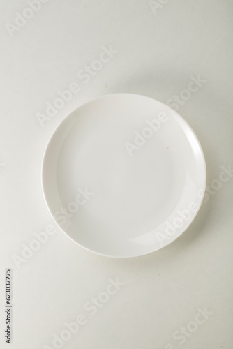 Plato blanco vacío  sobre fondo blanco. Vista cenital. Empty white plate on white background. overhead view.