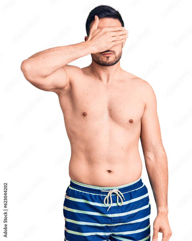 Young handsome man wearing swimwear covering eyes with hand, looking serious and sad. sightless, hiding and rejection concept Young handsome man wearing swimwear covering eyes with hand, looking serious and sad. sightless, hiding and rejection concept