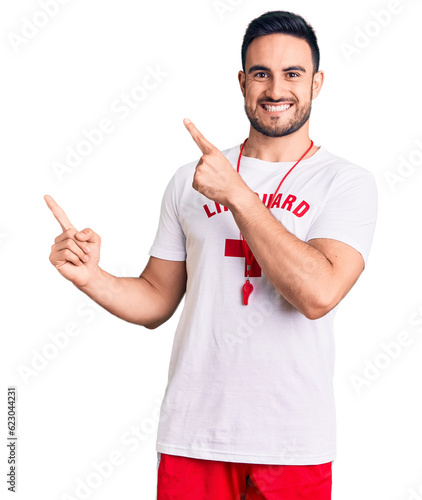 Young handsome man wearing lifeguard uniform smiling and looking at the camera pointing with two hands and fingers to the side.