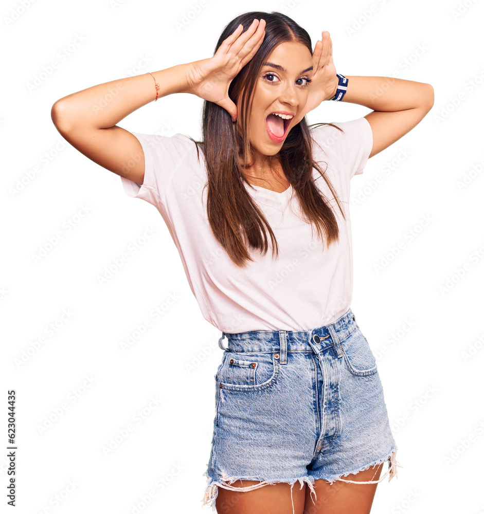 Young hispanic woman wearing casual white tshirt smiling cheerful playing peek a boo with hands showing face. surprised and exited Young hispanic woman wearing casual white tshirt smiling cheerful playing peek a boo with hands showing face. surprised and exited