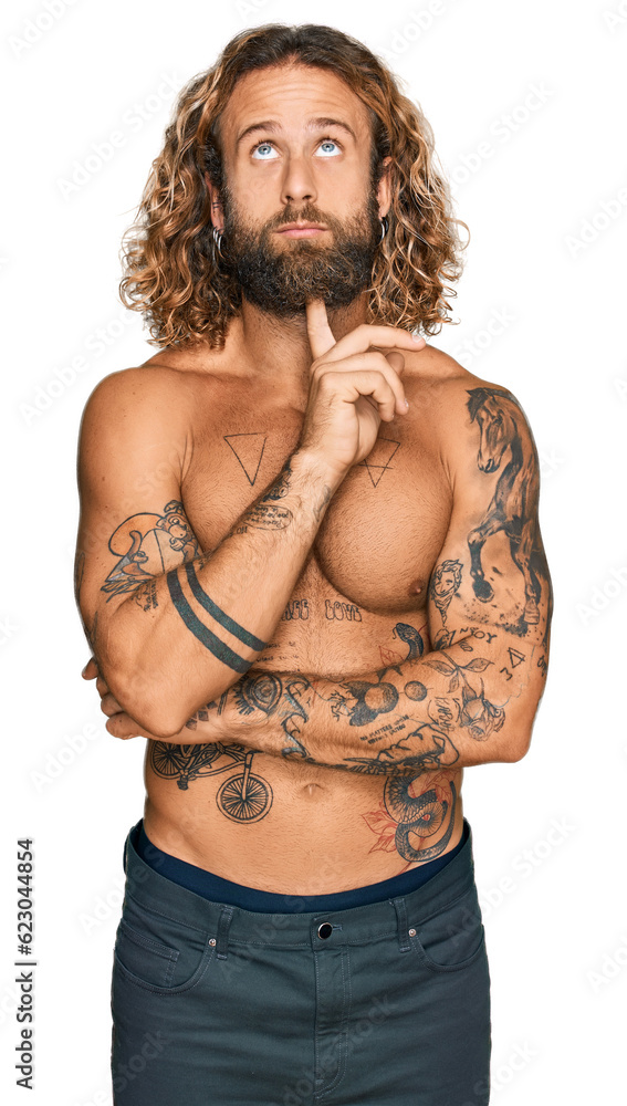 Fototapeta premium Handsome man with beard and long hair standing shirtless showing tattoos thinking concentrated about doubt with finger on chin and looking up wondering