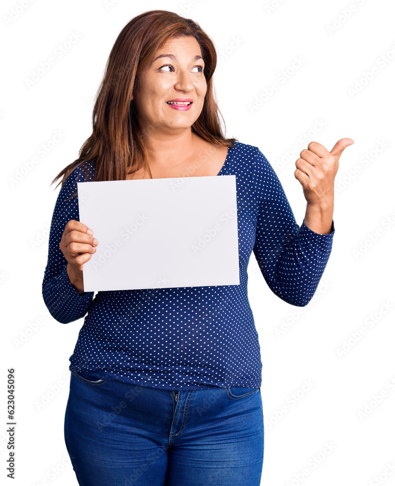 Middle age latin woman holding paper banner with blank space pointing thumb up to the side smiling happy with open mouth Middle age latin woman holding paper banner with blank space pointing thumb up to the side smiling happy with open mouth