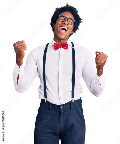 Handsome african american man with afro hair wearing hipster elegant look very happy and excited doing winner gesture with arms raised, smiling and screaming for success. celebration concept.