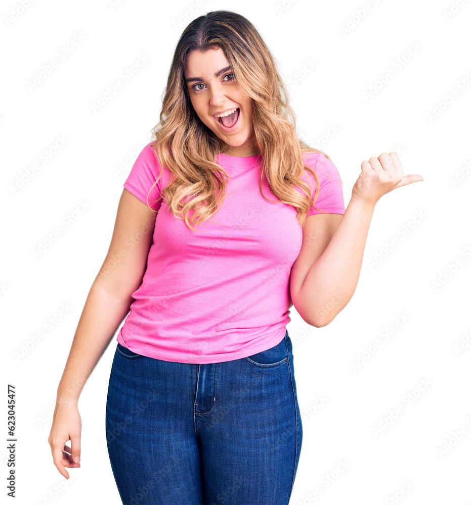 Young caucasian woman wearing sportswear smiling with happy face looking and pointing to the side with thumb up. Young caucasian woman wearing sportswear smiling with happy face looking and pointing to the side with thumb up.