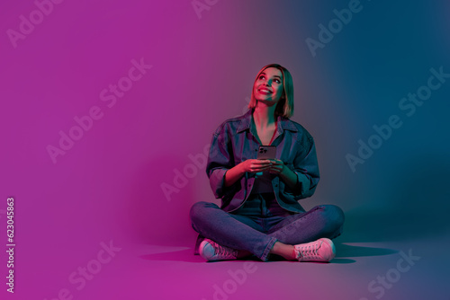 Photo of positive lady sitting using cell smart gadget online shopping on social network isolated gradient neon color background