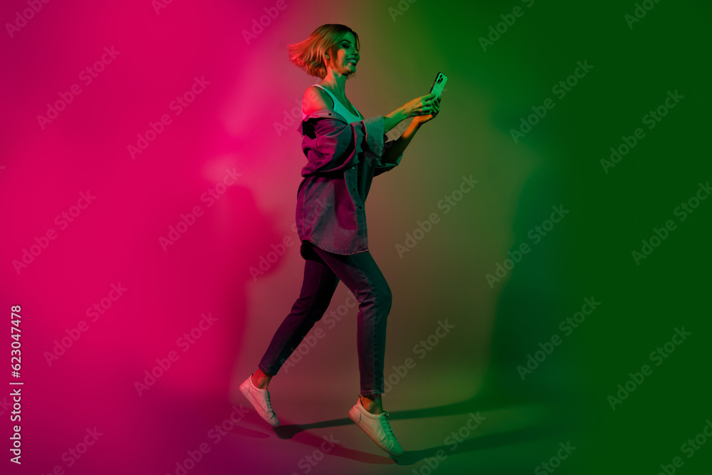 Full length photo of positive lady jump use smart gadget hurry buying tickets on club disco event isolated colorful neon background