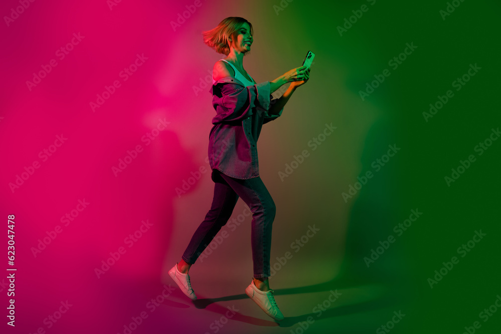 Full length photo of positive lady jump use smart gadget hurry buying tickets on club disco event isolated colorful neon background Full length photo of positive lady jump use smart gadget hurry buying tickets on club disco event isolated colorful neon background