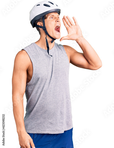 Young handsome man wearing bike helmet shouting and screaming loud to side with hand on mouth. communication concept. © Krakenimages.com