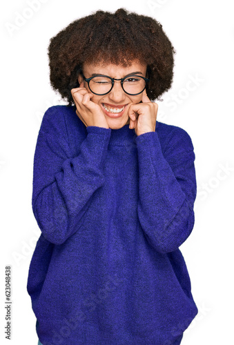 Young hispanic girl wearing casual winter sweater and glasses covering ears with fingers with annoyed expression for the noise of loud music. deaf concept.