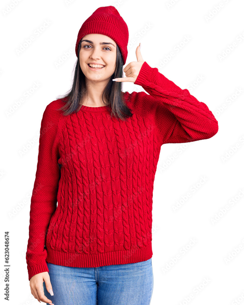 Young beautiful girl wearing sweater and wool cap smiling doing phone gesture with hand and fingers like talking on the telephone. communicating concepts. Young beautiful girl wearing sweater and wool cap smiling doing phone gesture with hand and fingers like talking on the telephone. communicating concepts.