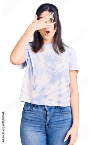 Young beautiful girl wearing casual t shirt peeking in shock covering face and eyes with hand, looking through fingers with embarrassed expression. © Krakenimages.com