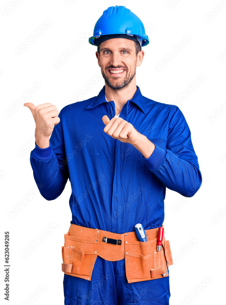 Young handsome man wearing worker uniform and hardhat pointing to the back behind with hand and thumbs up, smiling confident