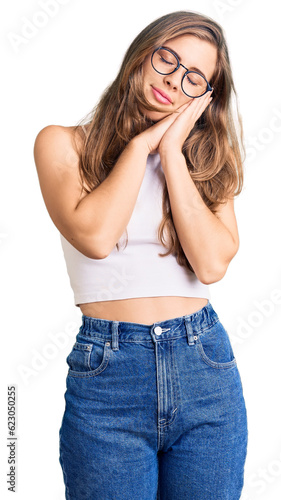 Beautiful caucasian young woman wearing casual clothes and glasses sleeping tired dreaming and posing with hands together while smiling with closed eyes.