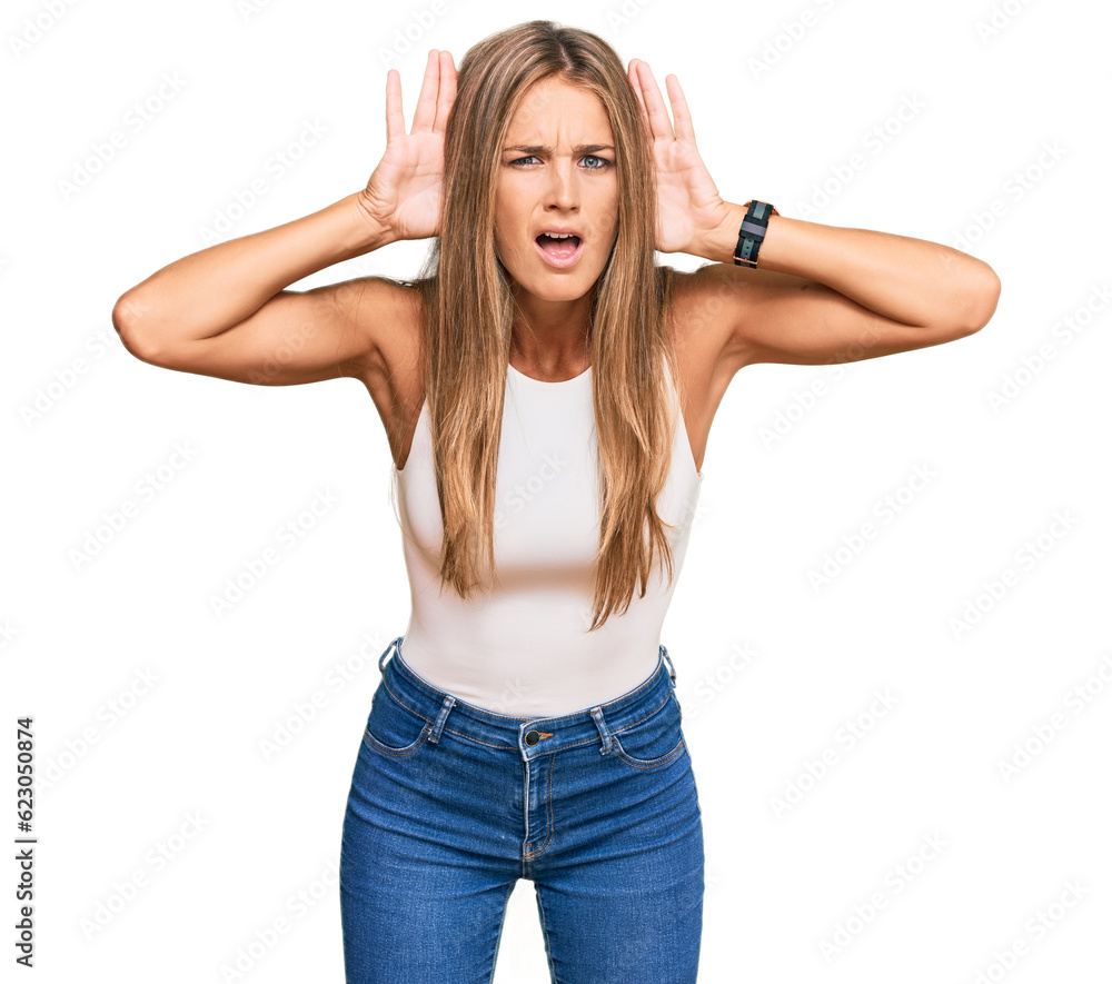 Young blonde woman wearing casual style with sleeveless shirt trying to hear both hands on ear gesture, curious for gossip. hearing problem, deaf
