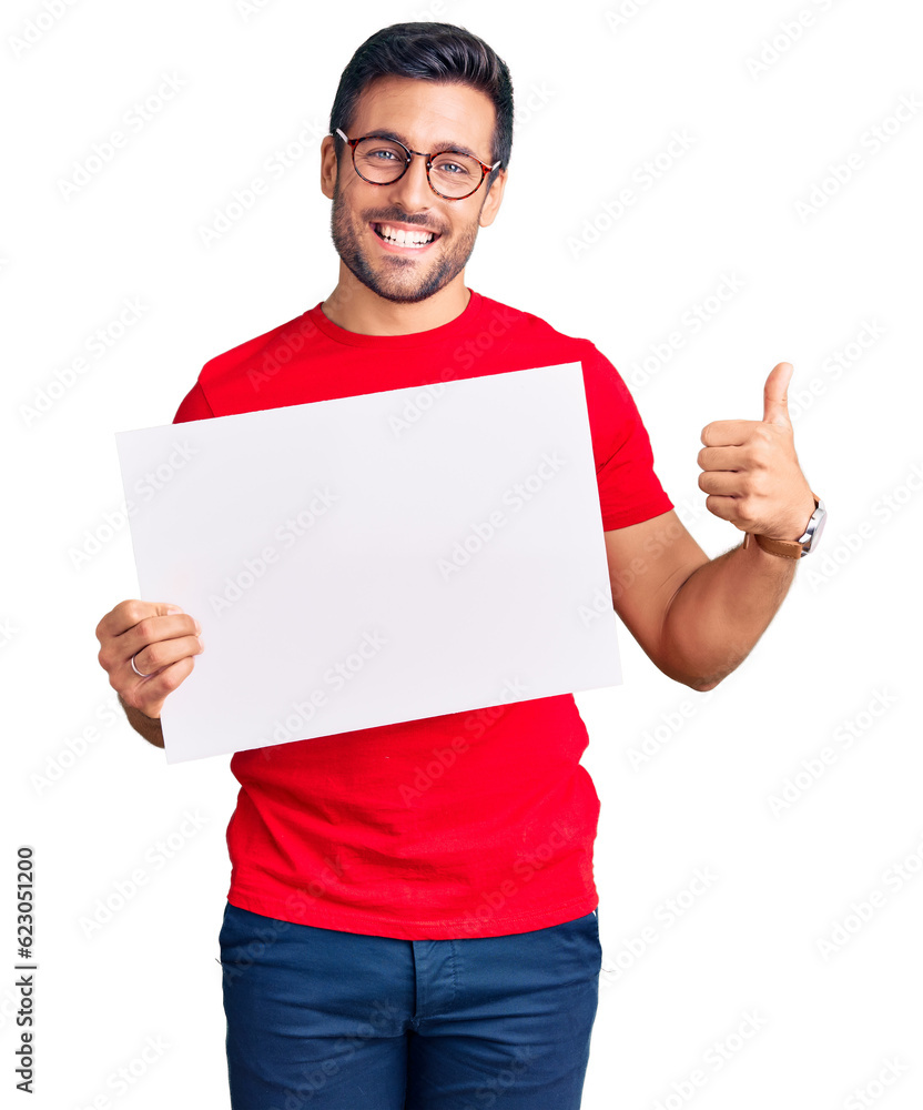 Young hispanic man holding blank empty banner smiling happy and positive, thumb up doing excellent and approval sign Young hispanic man holding blank empty banner smiling happy and positive, thumb up doing excellent and approval sign