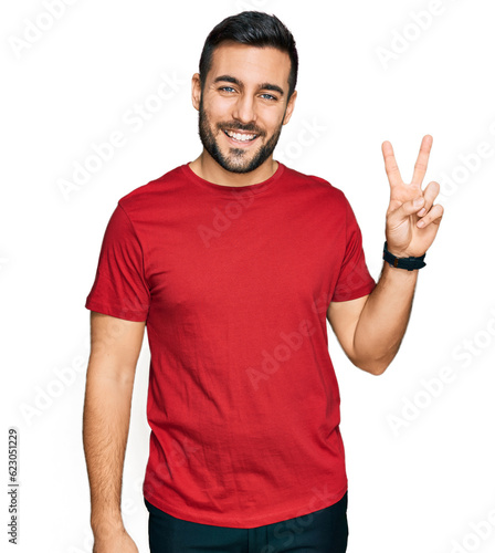 Young hispanic man wearing casual clothes smiling with happy face winking at the camera doing victory sign. number two.