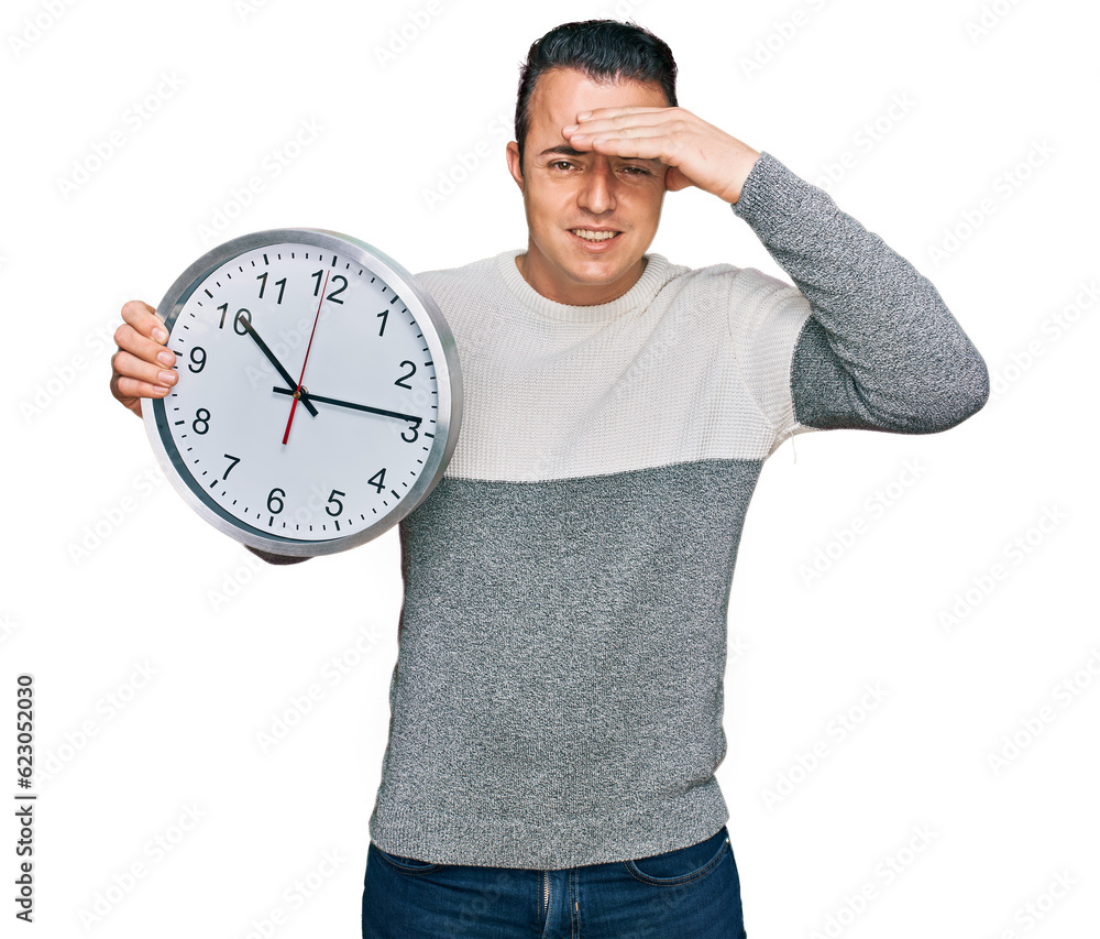 Handsome young man holding big clock stressed and frustrated with hand on head, surprised and angry face Handsome young man holding big clock stressed and frustrated with hand on head, surprised and angry face